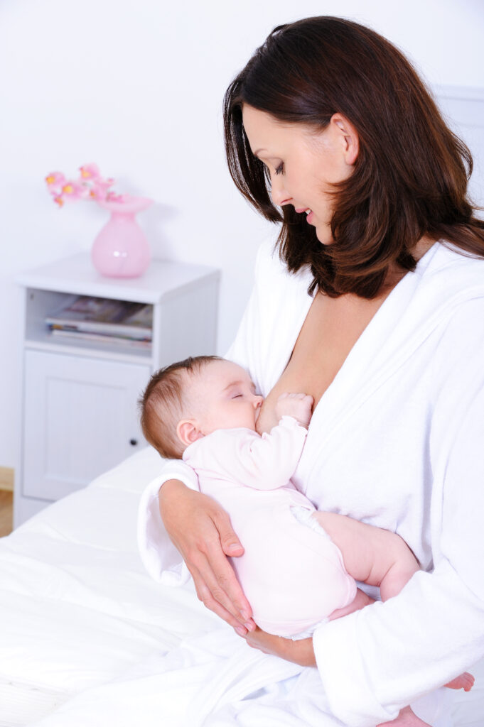 Portrait of young mother feeding her newborn baby with breast - indoors